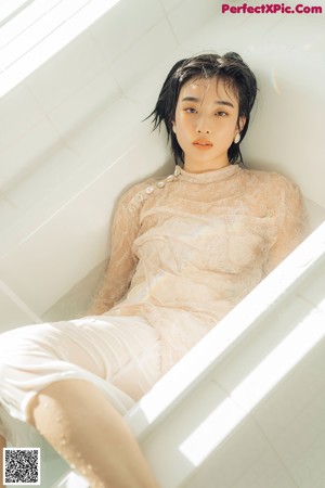 A woman sitting on the floor in a yellow top and white skirt.