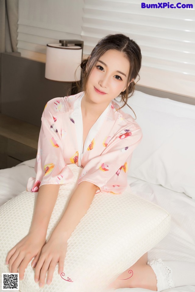 A woman sitting on a bed wearing a pink robe.