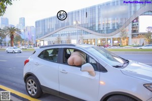 A naked woman wearing a face mask standing next to a car.