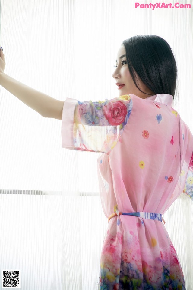 A woman in a pink kimono standing by a window.