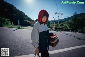 A woman in a red hooded outfit is sitting in the woods.