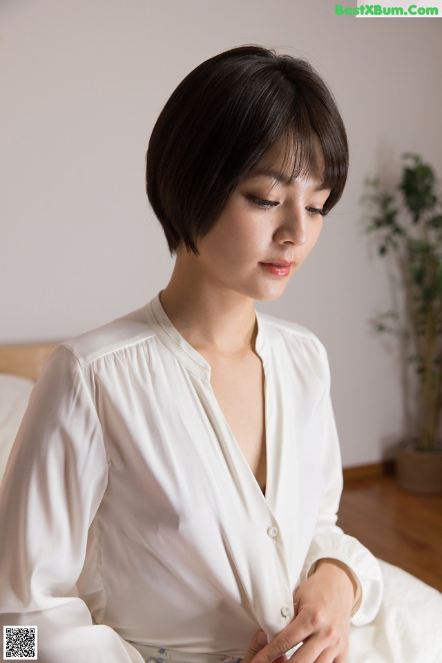 A woman in a white shirt sitting on a bed.