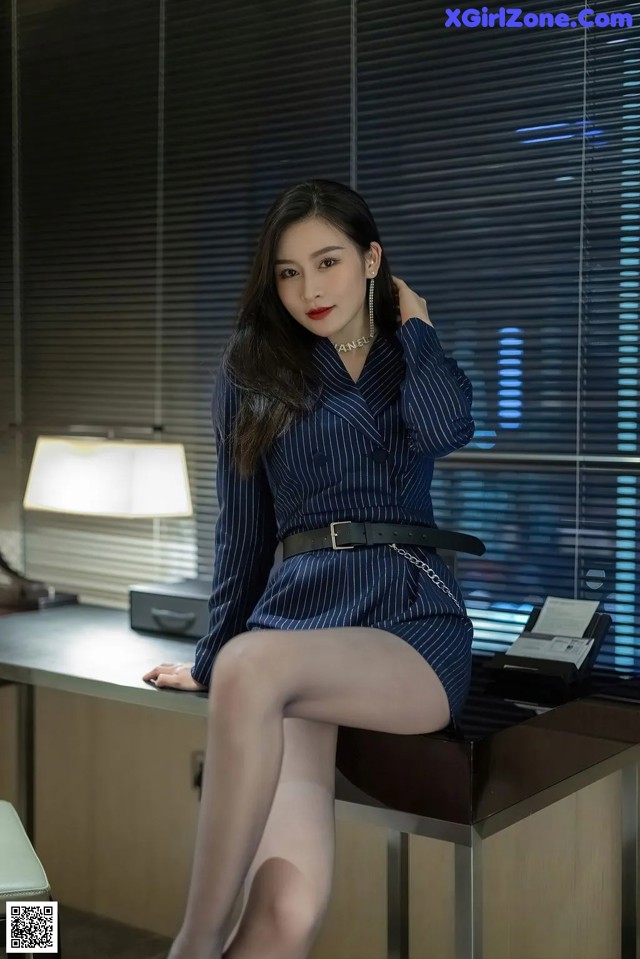 A woman sitting on top of a desk next to a lamp.