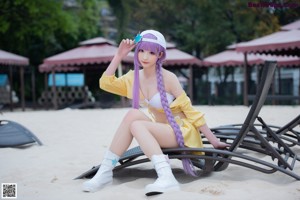 A woman with long purple hair sitting on an inflatable ring on the beach.