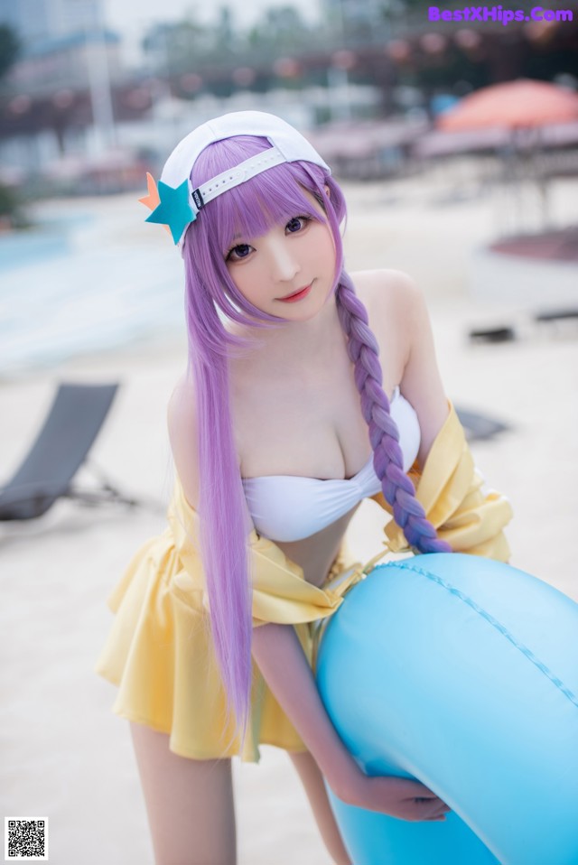 A woman in a yellow dress holding a blue ball on a beach.