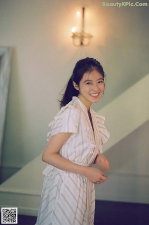 A woman in a black dress leaning against a wall.