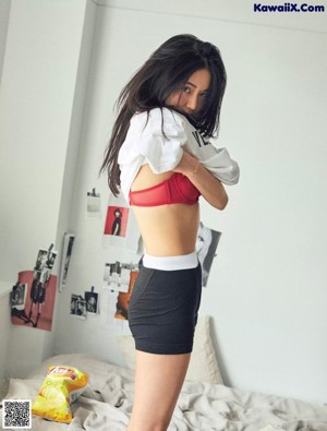 A woman sitting on a window sill in a white shirt and shorts.