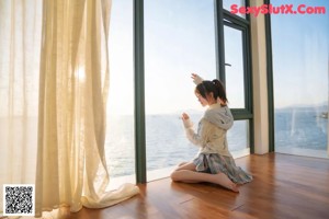A woman standing by a window looking out at the ocean.