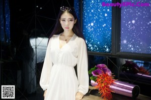A woman in a long white dress standing on a sidewalk.