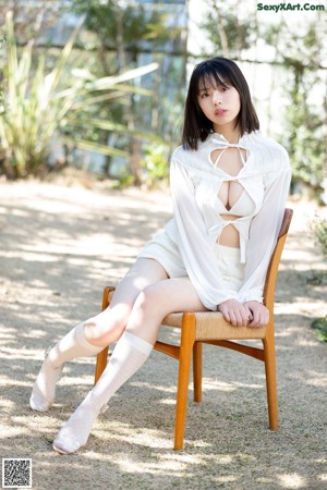 A woman in a white shirt and shorts sitting on a bed.