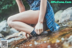 A woman in a blue top and plaid skirt standing in a stream.