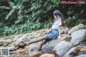 A woman in a blue and white plaid skirt is standing in a stream.