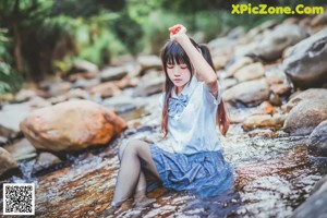 A woman standing on a rock in a stream.