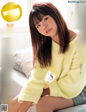 A woman in a yellow sweater sitting on a bed.