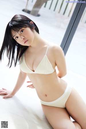 A young woman sitting on a wooden floor with her hands on her chin.