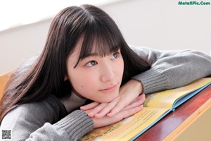 A young woman sitting on a desk in a school uniform.