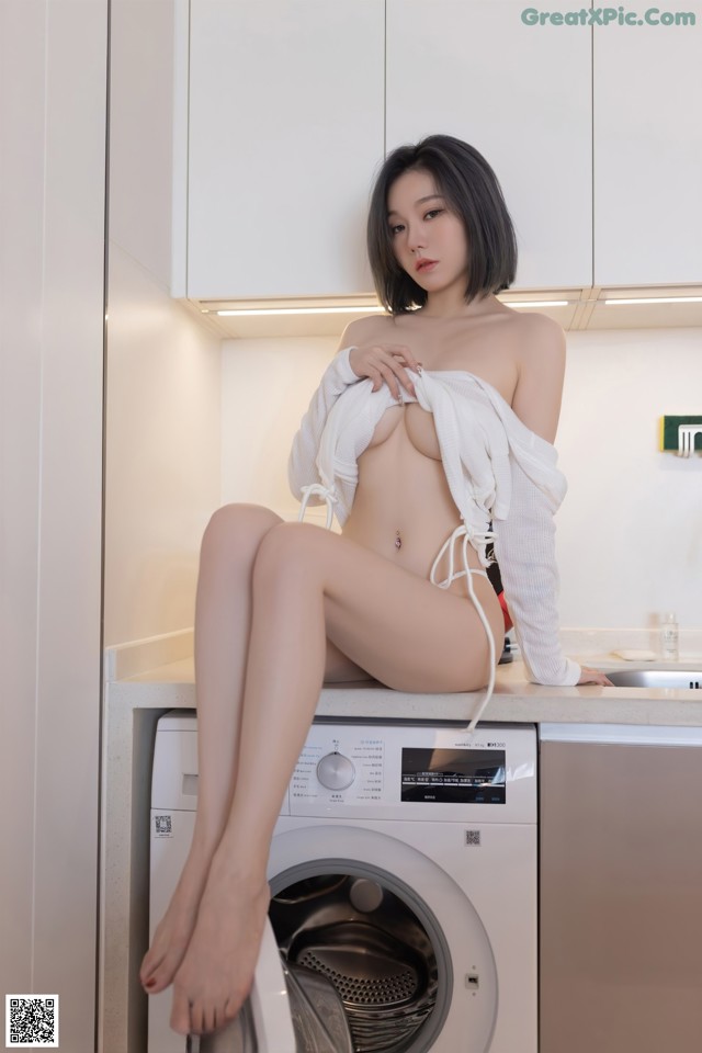 A woman sitting on top of a washing machine in a kitchen.