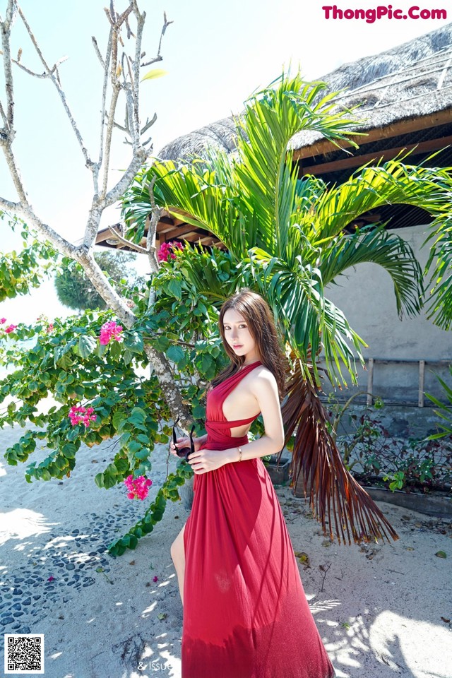 A woman in a red dress standing next to a palm tree.