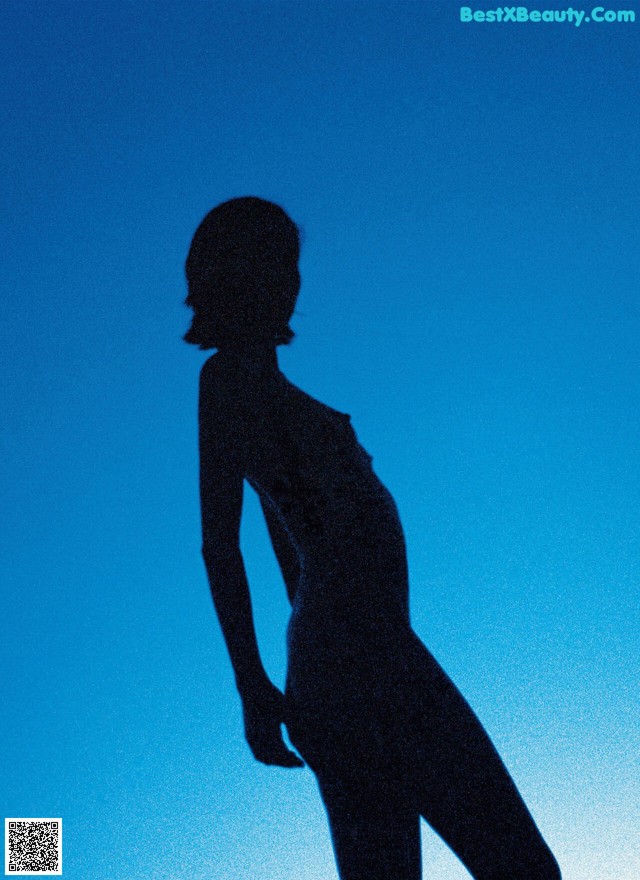 A silhouette of a woman standing in front of a blue sky.