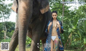 A woman in a long dress standing next to an elephant.