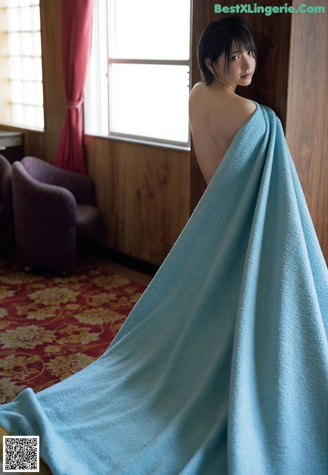 A woman wrapped in a blue towel standing in a room.