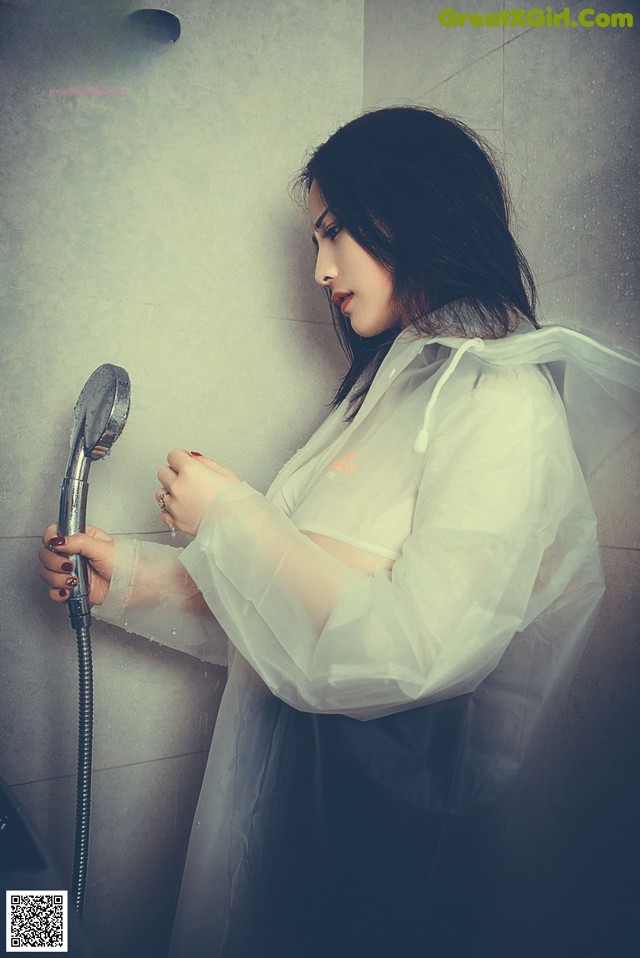 A woman in a white raincoat holding a shower head.