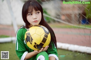 A young woman holding a soccer ball in front of a goal.