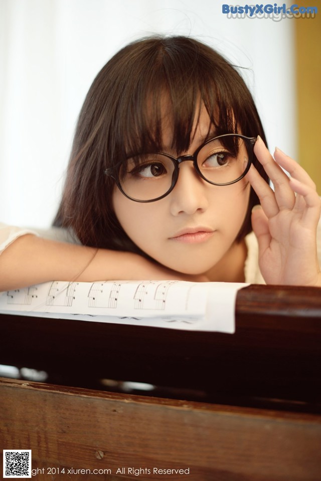 A young woman wearing glasses sitting at a piano.