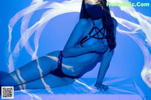 A woman in a black thong sitting on a wooden floor.