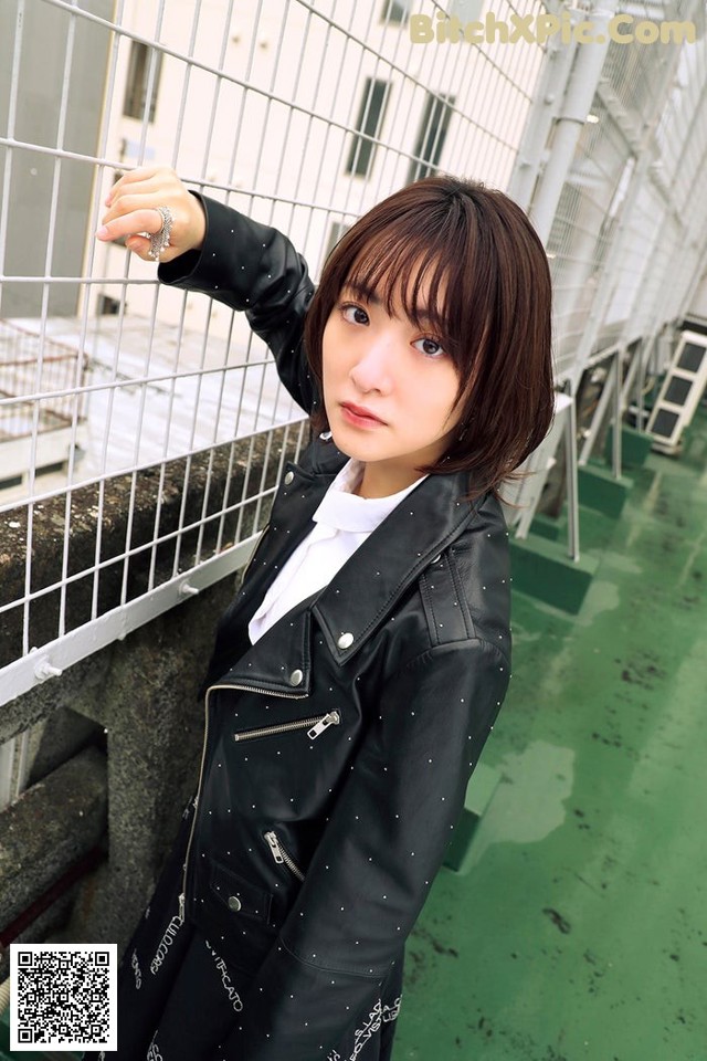 A woman in a black leather jacket leaning against a fence.