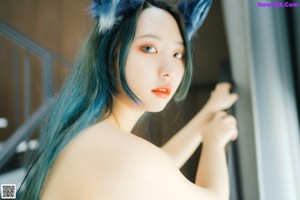 A naked woman with blue hair and cat ears sitting on the floor.