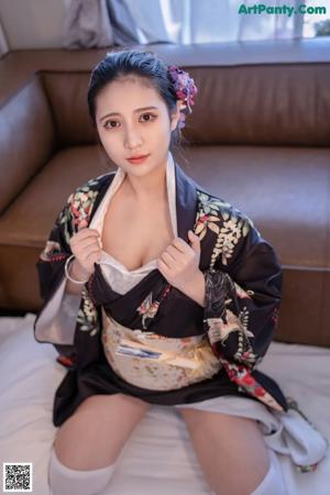 A woman in a kimono sitting on a bed holding a fan.