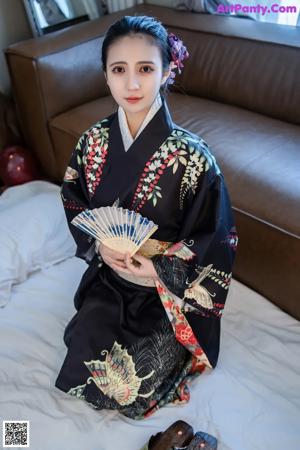 A woman in a black kimono sitting on a bed holding chopsticks.