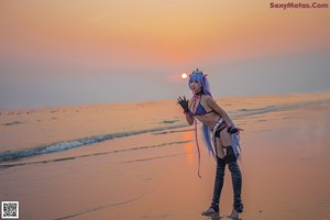 A woman with long blue hair standing on a beach.