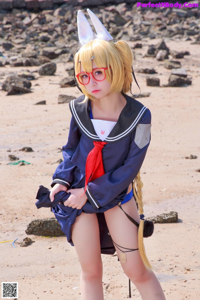 A woman in a sailor outfit is posing on the beach.