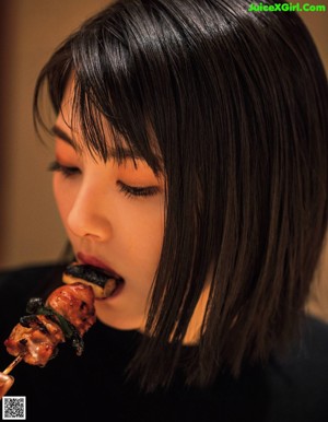 A woman eating a piece of meat on a stick.