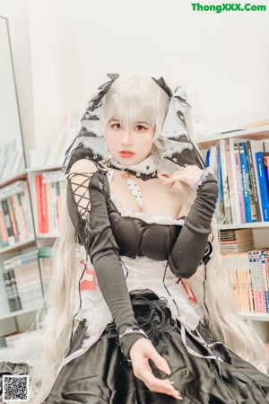 A woman in a black and white dress sitting in front of a book shelf.