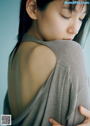 A woman sitting on a window sill wearing a blue sweater.