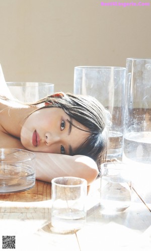 A naked woman laying on a wooden table next to two glasses of water.