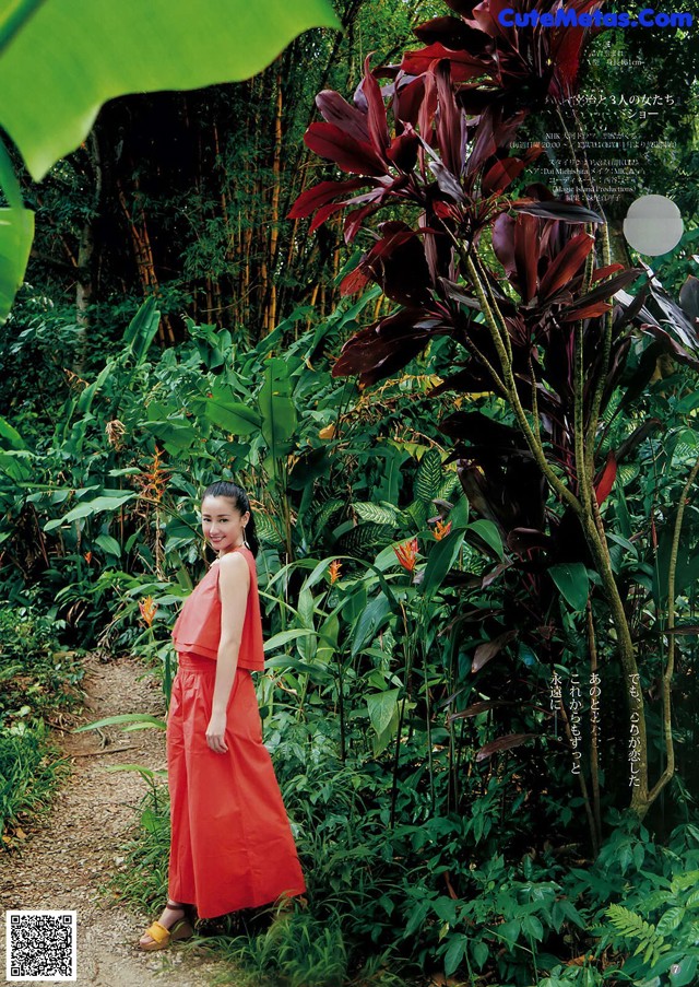 A woman in a red dress standing in the middle of a forest.