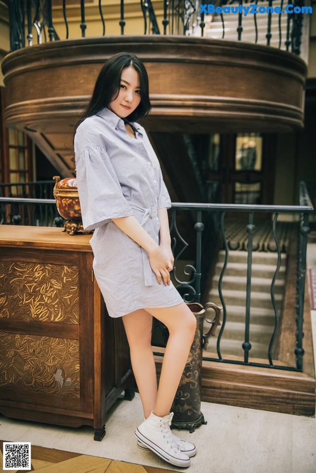 A woman in a blue shirt dress and white sneakers posing for a picture.