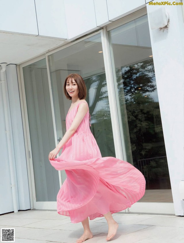 A woman in a pink dress is walking outside of a building.