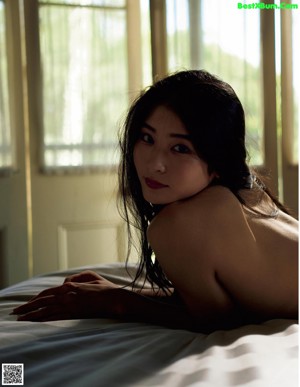 A naked asian woman sitting on a bed in a bedroom.