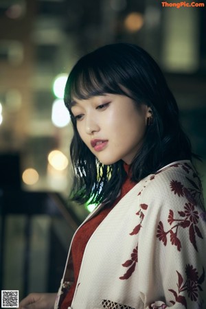 A woman in a kimono sitting on a chair with her hand on her chin.