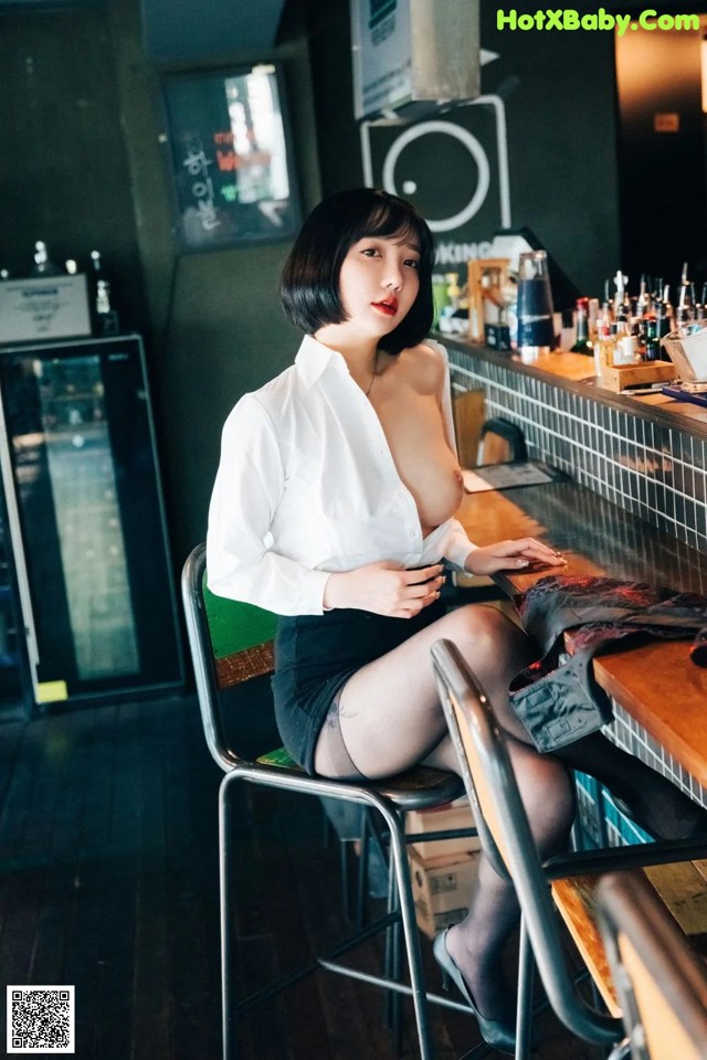 A woman sitting at a bar in a white shirt and black skirt.