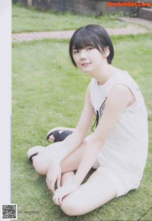 A woman sitting on the floor wearing a white shirt and shorts.