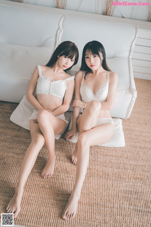 Two young women sitting on a white couch.