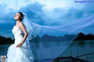 A woman in a wedding dress sitting on a dock.