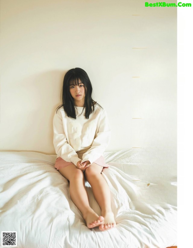 A woman sitting on top of a bed in a white shirt.